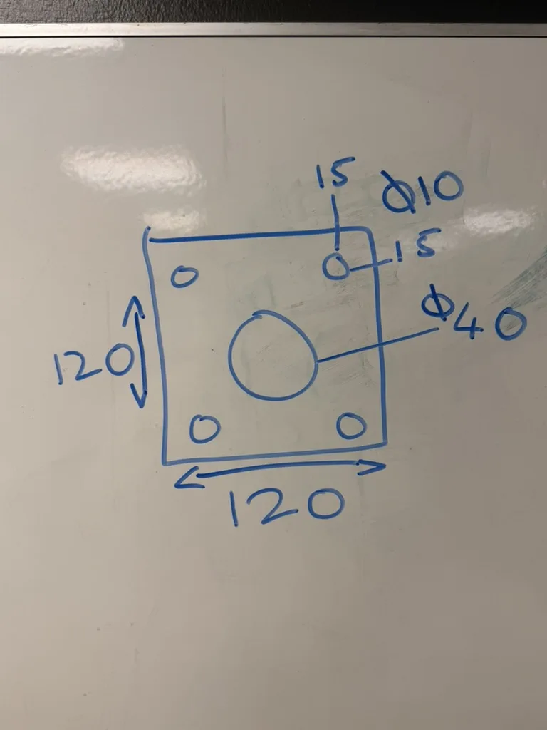 A phone photo of a plate sketched in blue marker on a whiteboard, taken at an angle: a 120 × 120 square with four small corner holes marked Ø10 at 15 from the edges, and a Ø40 hole in the middle, not drawn to scale